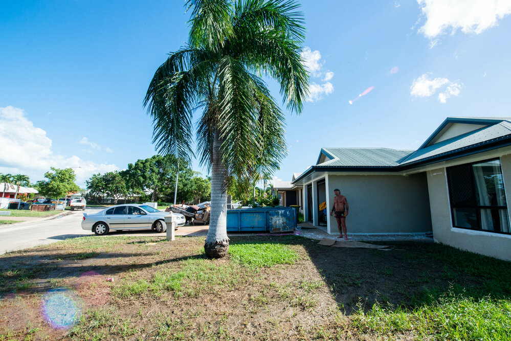 Resident standing in front of flood affected home with skip bin located on driveway, Idalia, 2019