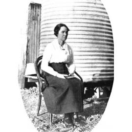 Miss Cummins seated before water tank, ca 1921 