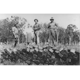 Henry Hussey and Vince Elliot and wife, and Sam Clark, standing on a pile of railway sleepers, at Moongobulla station, ca 1930 