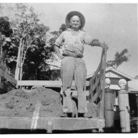 Mr Cavill on back of a truck parked next to two petrol pumps with Cavill's Guest House in the background ca 1940