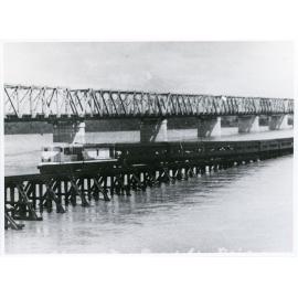 Train number 13 "Pony Express" crossing low level Burdekin river railway bridge during March flood, 1957. The new high level bridge is in the background