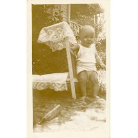 Baby photographed in the garden with a doll's bed, Townsville