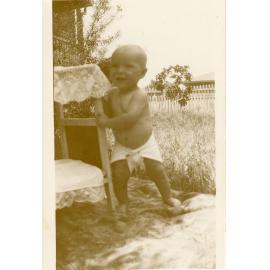 Baby photographed in the garden with a doll's bed, Townsville