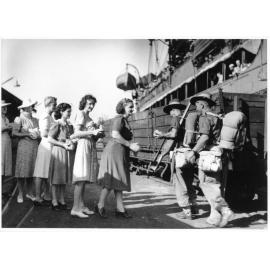 Members of the Townsville Branch of the Australian Comforts Fund distributing bags of fruit to soldiers of the 5th Australian Division as they disembark from HMT Katoomba on the 25th March 1945