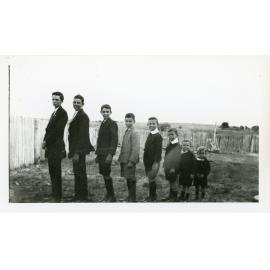 Eight unidentified boys, facing sideways, posing for a photograph