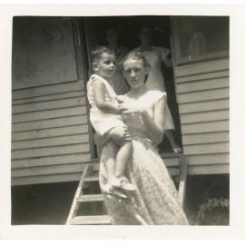 Girl posing with young Neil Ballment and mother Ruth Ballment in doorway, Magnetic Island, Townsville, [1950s]