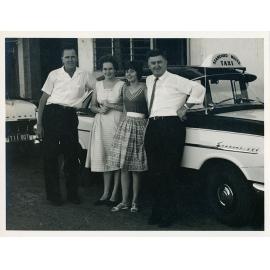 A group of four people beside a Standard White Taxi