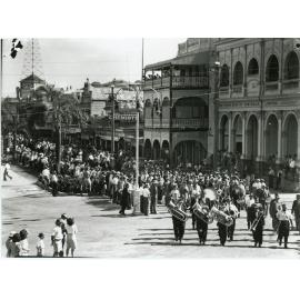 Procession of people following a brass band in Flinders Street after the peace announcement, Townsville, 15th August 1945