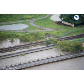 People gather on riverbank to watch water level skirt under Rooney's Bridge, aerial photograph during floods, 2019. 